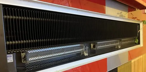An over-door terminal in service in a commercial interior: finned coil above, quartz radiant elements behind mesh g