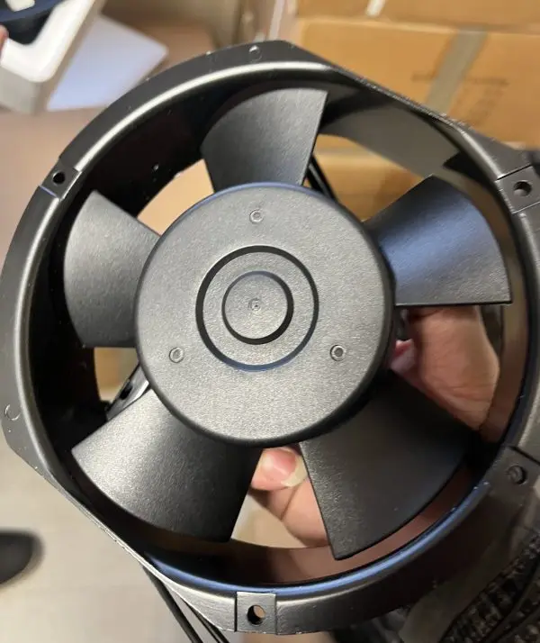 Close-up of a compact metal-framed axial fan with a five-blade impeller and lead wires, unpacked and held for inspe