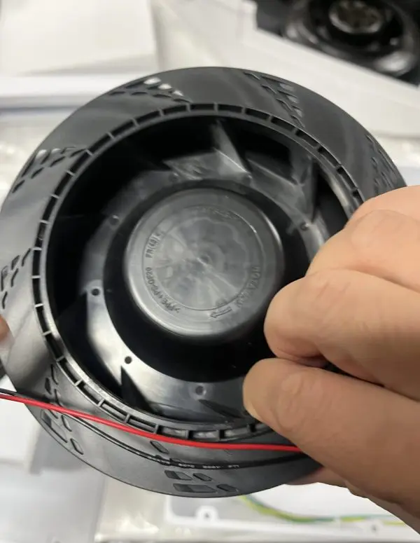 Close-up of a black plastic centrifugal blower wheel with an integrated motor and red/black lead wires, held in han