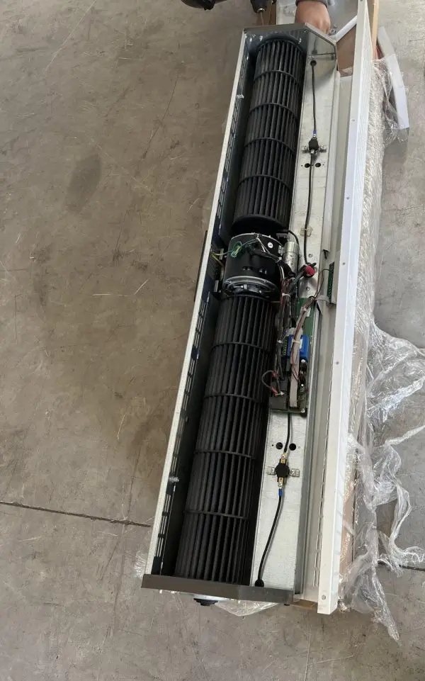 An air-curtain body opened up on a workshop floor, with the front panel removed to expose the internals: two long c