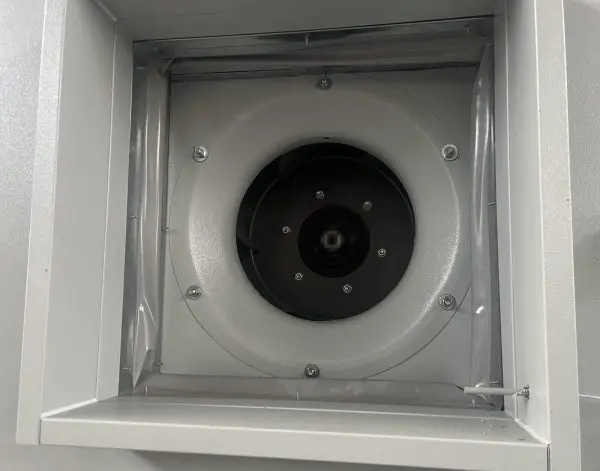 A backward-curved centrifugal impeller mounted behind the inlet cone inside a sheet-metal air-handling cabinet, pho